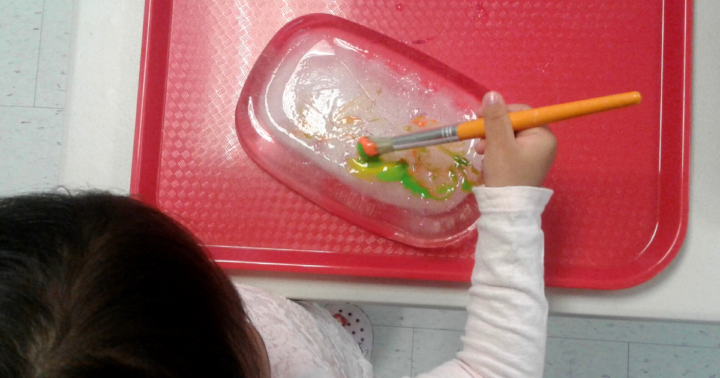 Child uses a paint brush to paint on a block of ice.