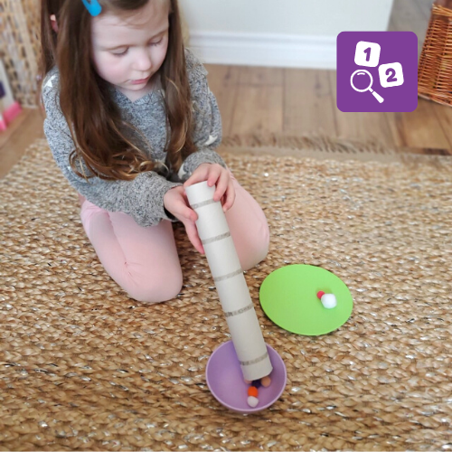 Child uses a cardboard tube as a ramp for craft pom poms.