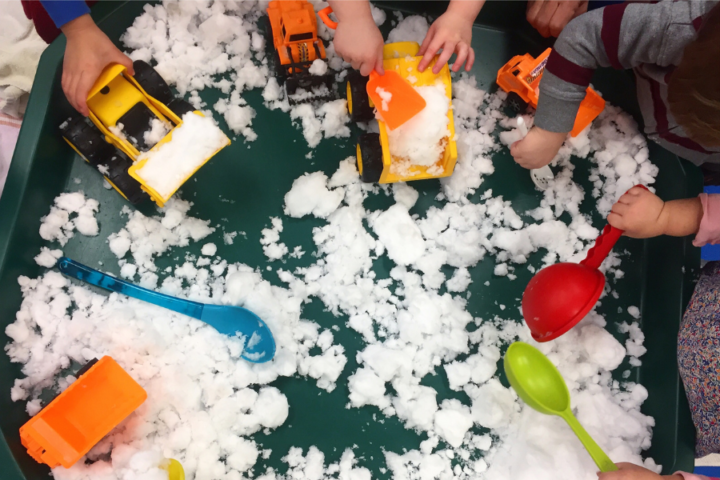Large tray filled with snow, toy trucks, and scoops.